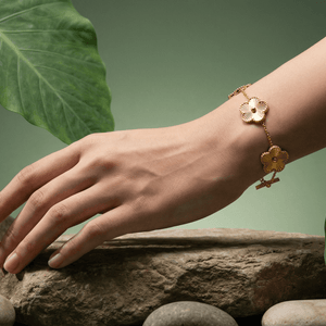 A hand wearing a Flower Charm Bracelet, surrounded by stones and green leaves, showcasing elegant floral jewelry.