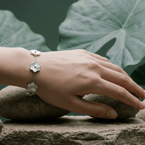 Flower Charm Bracelet worn on a hand resting on stones with green leaves in the background.