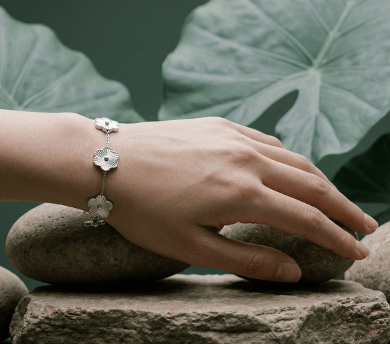 Flower Charm Bracelet worn on a hand resting on stones with green leaves in the background.